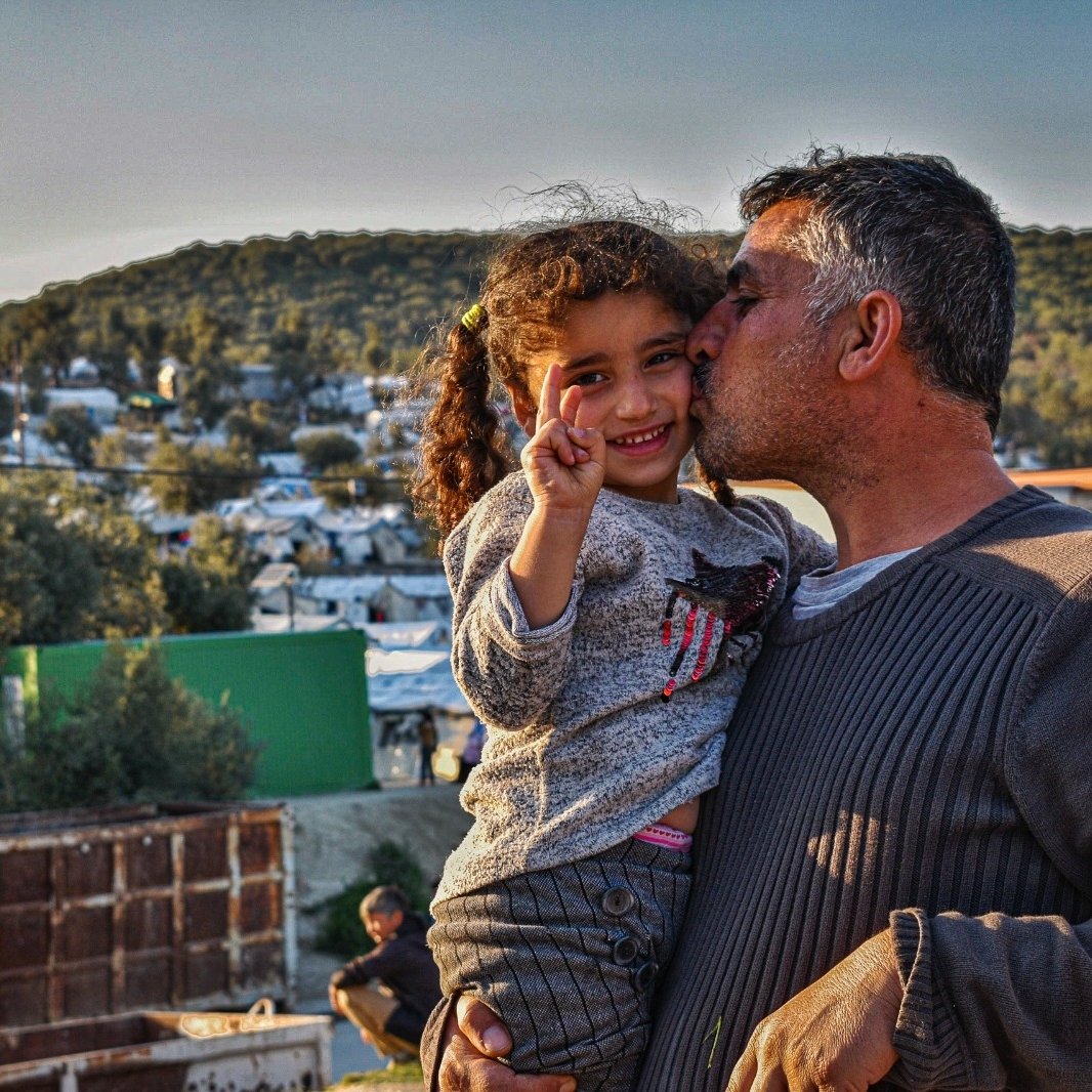 Father kisses the cheek of his smiling daughter as he holds her