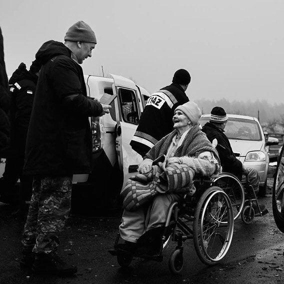 Abled-people helping old people in wheelchairs evacuate dangerous area. They are placed between cars and checking documentation. They are wearing winter clothes and are covered with blankets. photo credit: Костянтин і Влада Ліберови