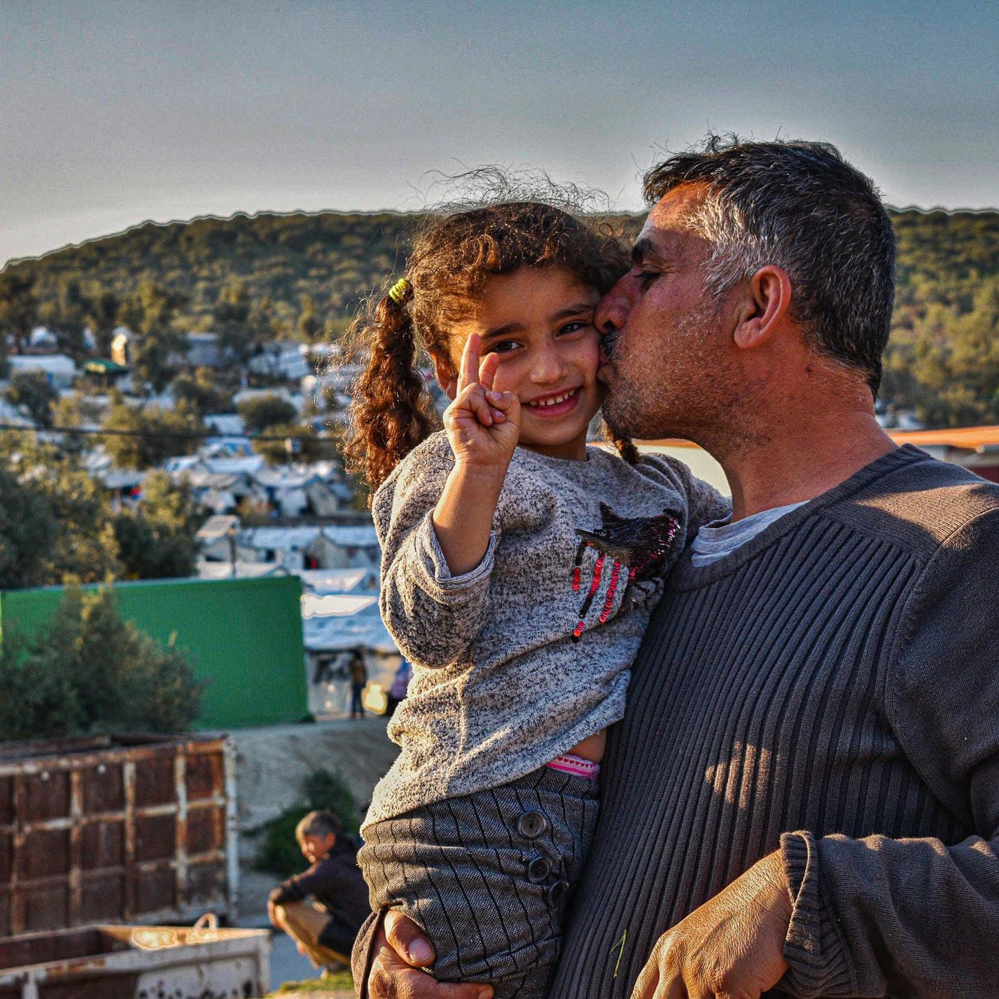 Father holds child in front of a camp