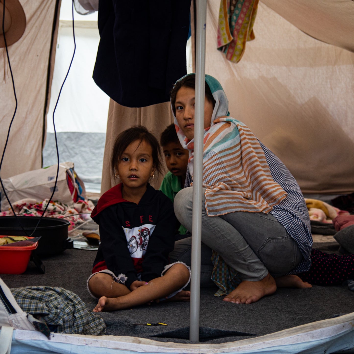 A woman and her daughter in a tent with clothes lying around.