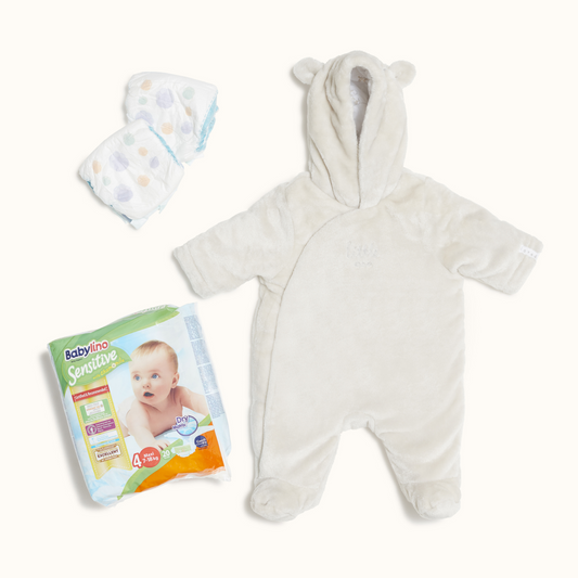 A fluffy babygrow with a hoodie and animal ears laying flat. Next to it towards the bottom left there is a large pack of 12 nappies, and in the top left there are 2 unopened nappies. 