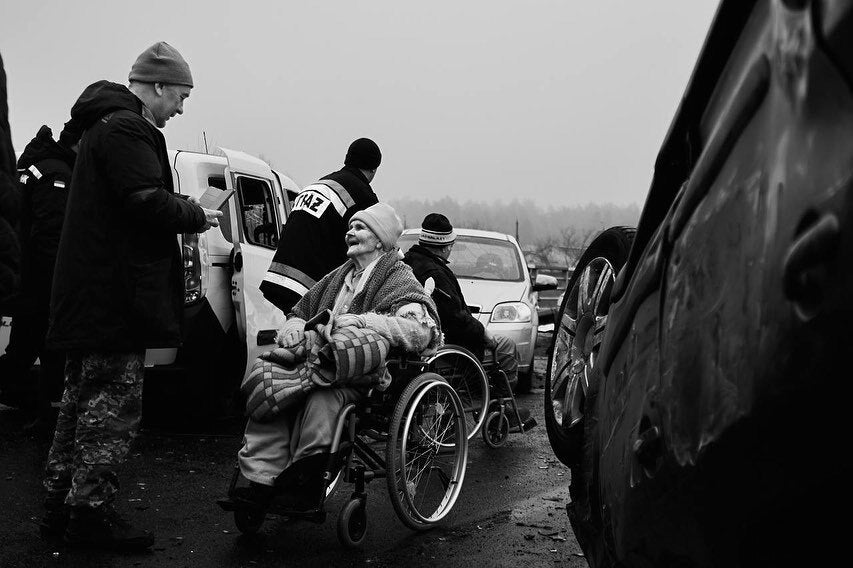 Abled-people helping old people in wheelchairs evacuate dangerous area. They are placed between cars and checking documentation. They are wearing winter clothes and are covered with blankets. photo credit: Костянтин і Влада Ліберови 