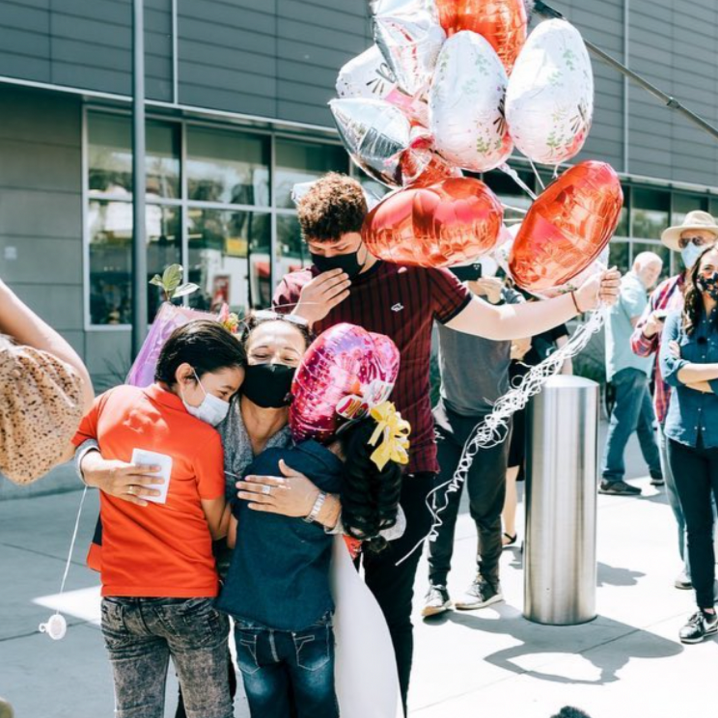 Mother reuniting with her 2 young children, and a man holding balloons behind.
