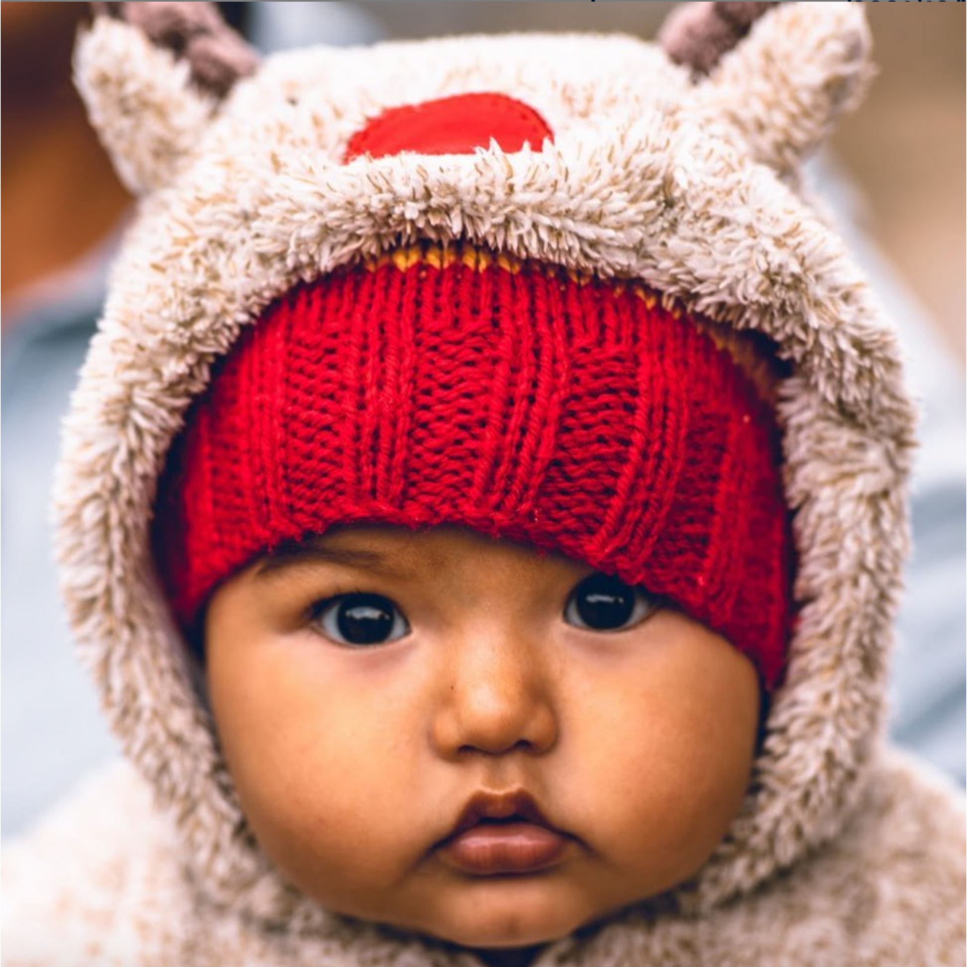 Close shot of a baby's face wearing a warm hat and covered with a fluffy hoodie.