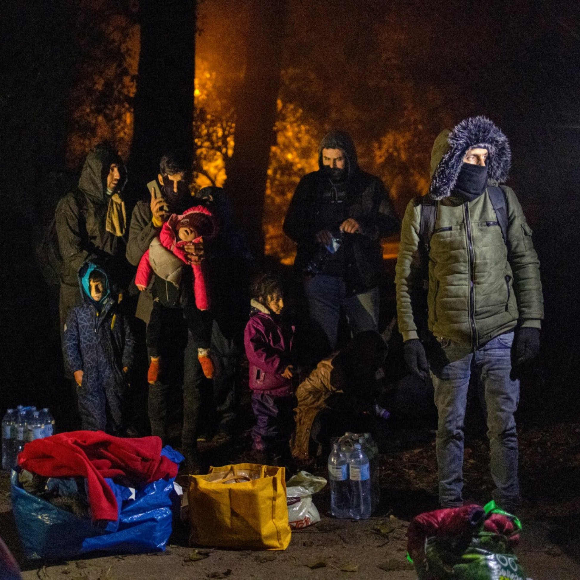 Refugees queueing up at night with lugagge on the floor.
