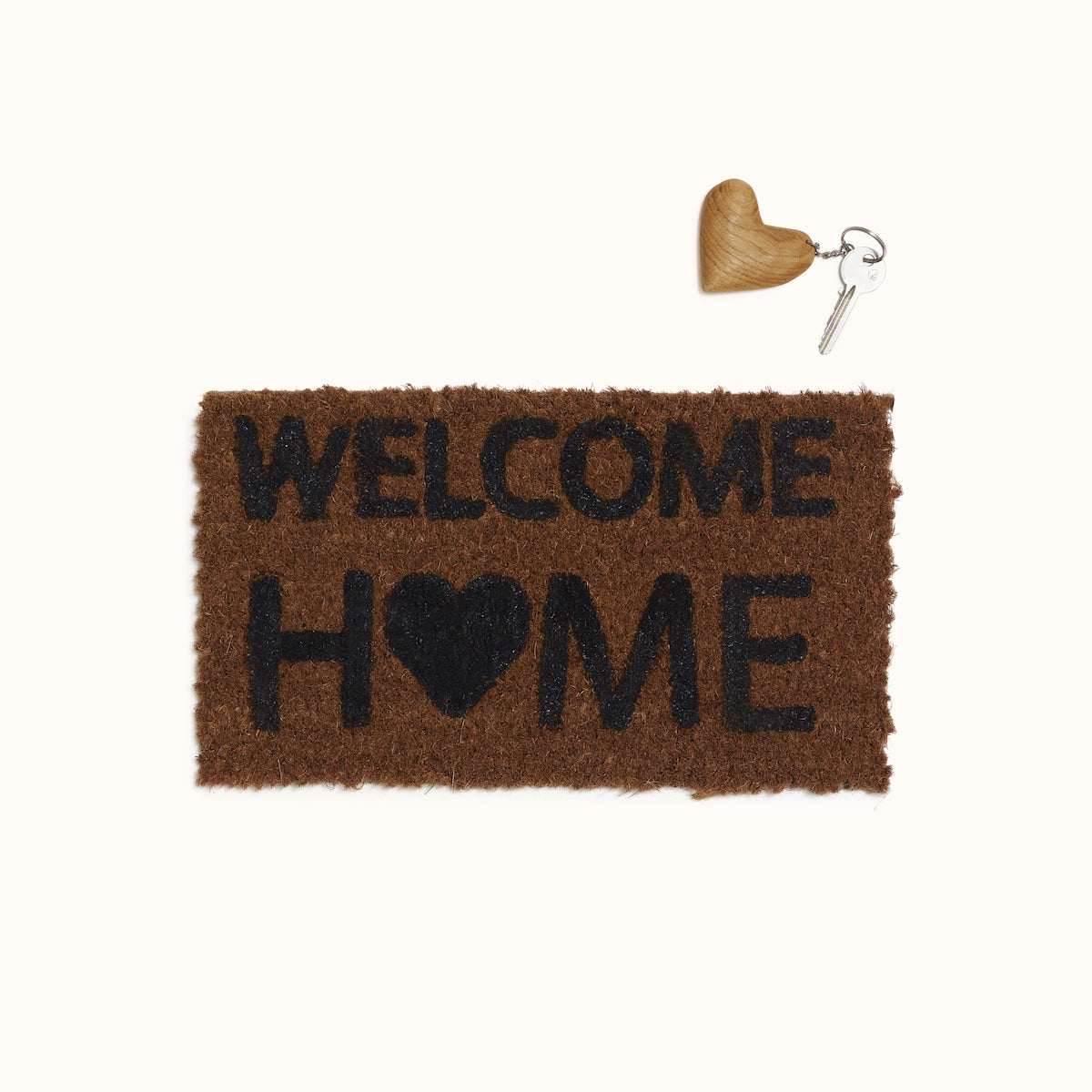 A coir entrance mat with the text Welcome Home, and a key with a wooden keyring attached to it on the top right side of the mat.